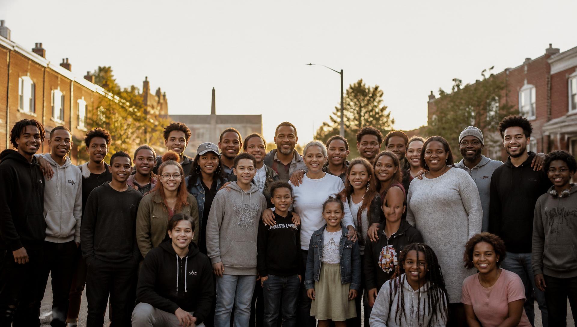 A large multigenerational Maryland community group gathered on a neighborhood block at golden hour, smiling together.